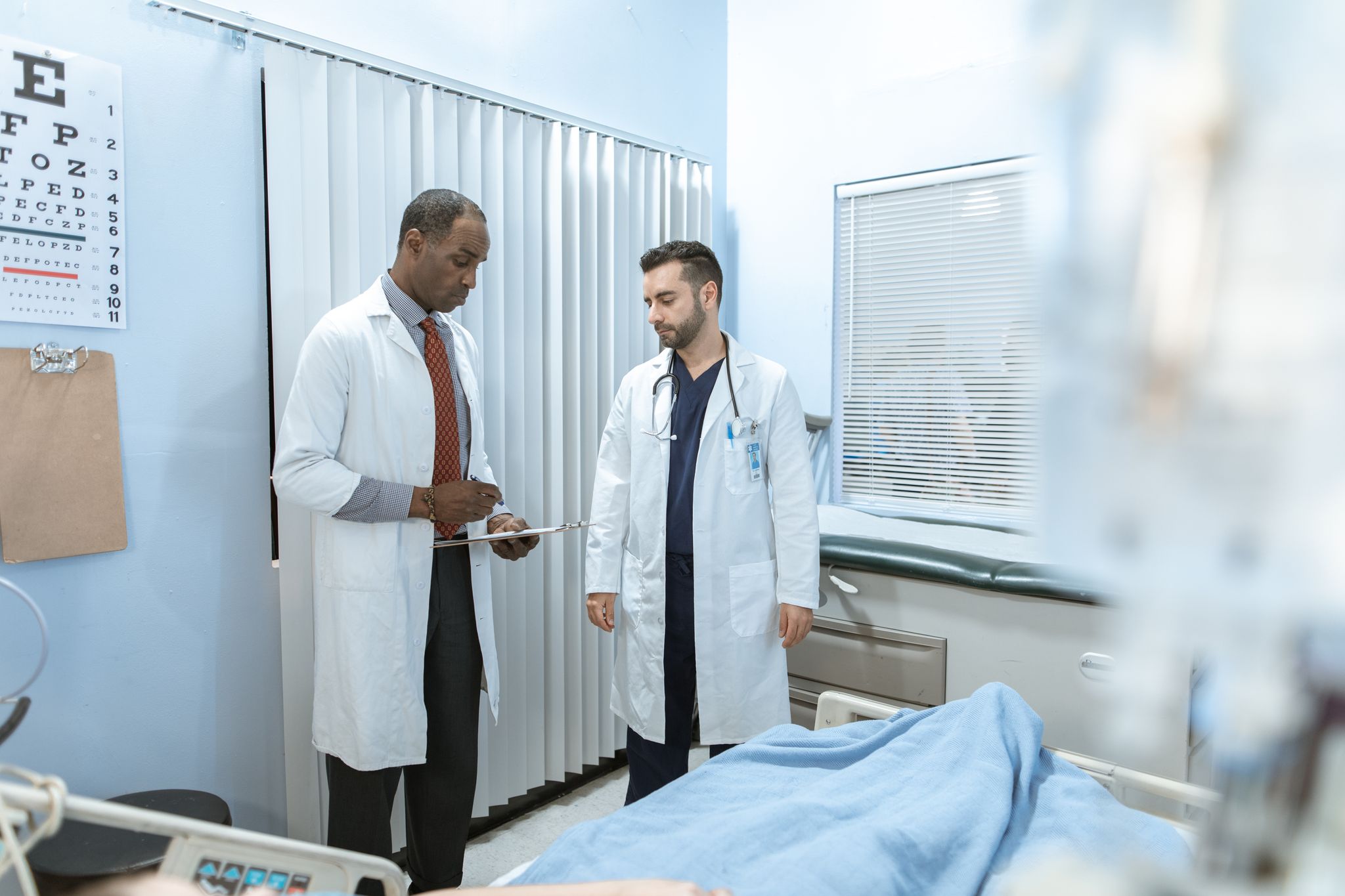Two doctors review a patient's chart in a hospital room, focusing on healthcare cooperation and medical care.